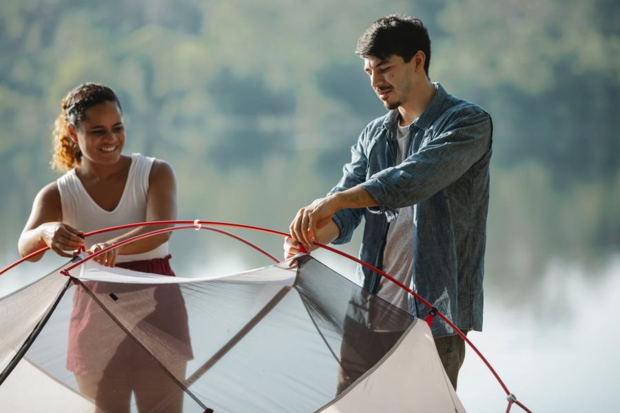 couple of travelers putting up tent near pond